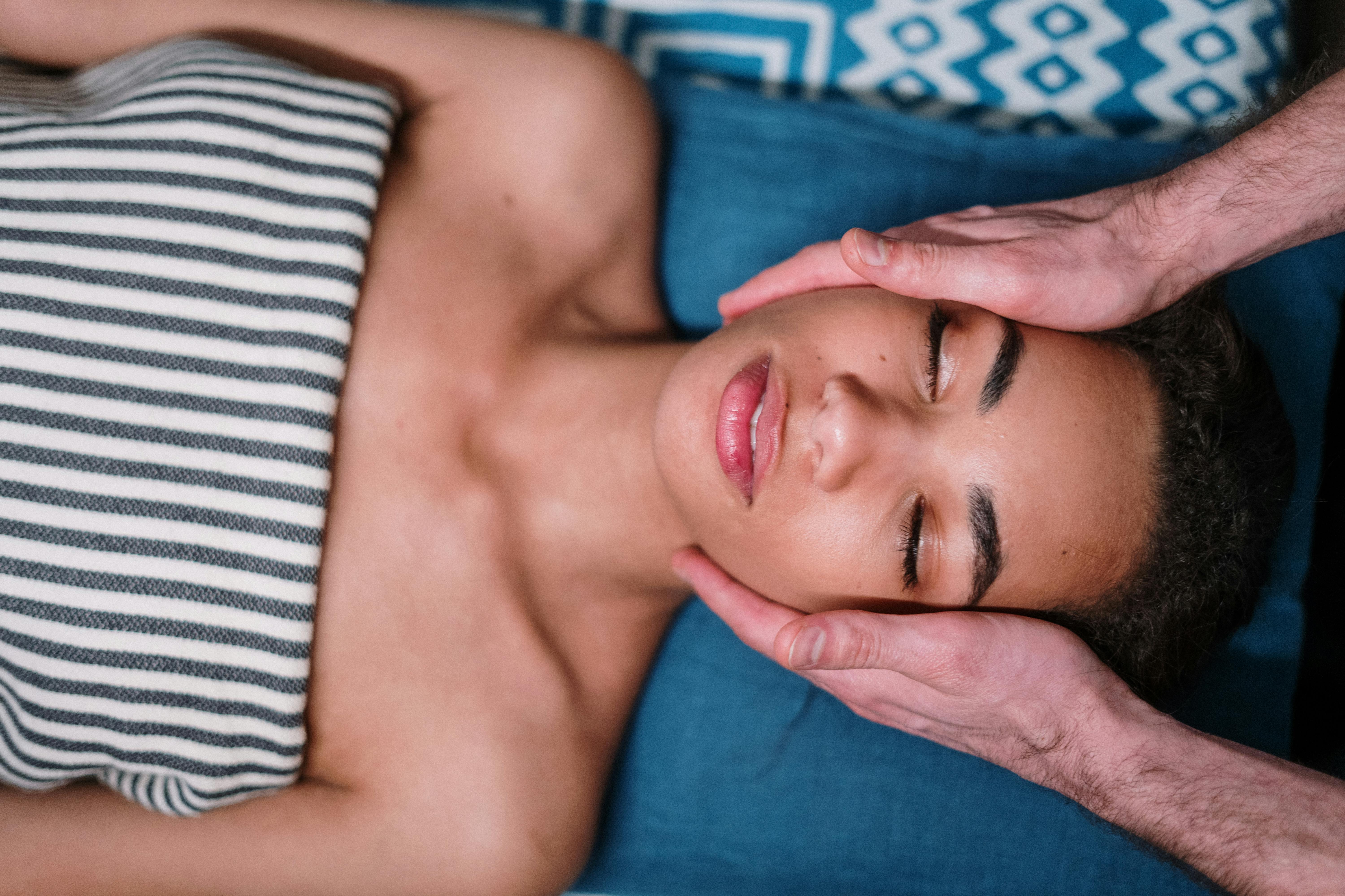 Mulher deitada de olhos fechados a receber uma massagem de relaxamento nos ombros